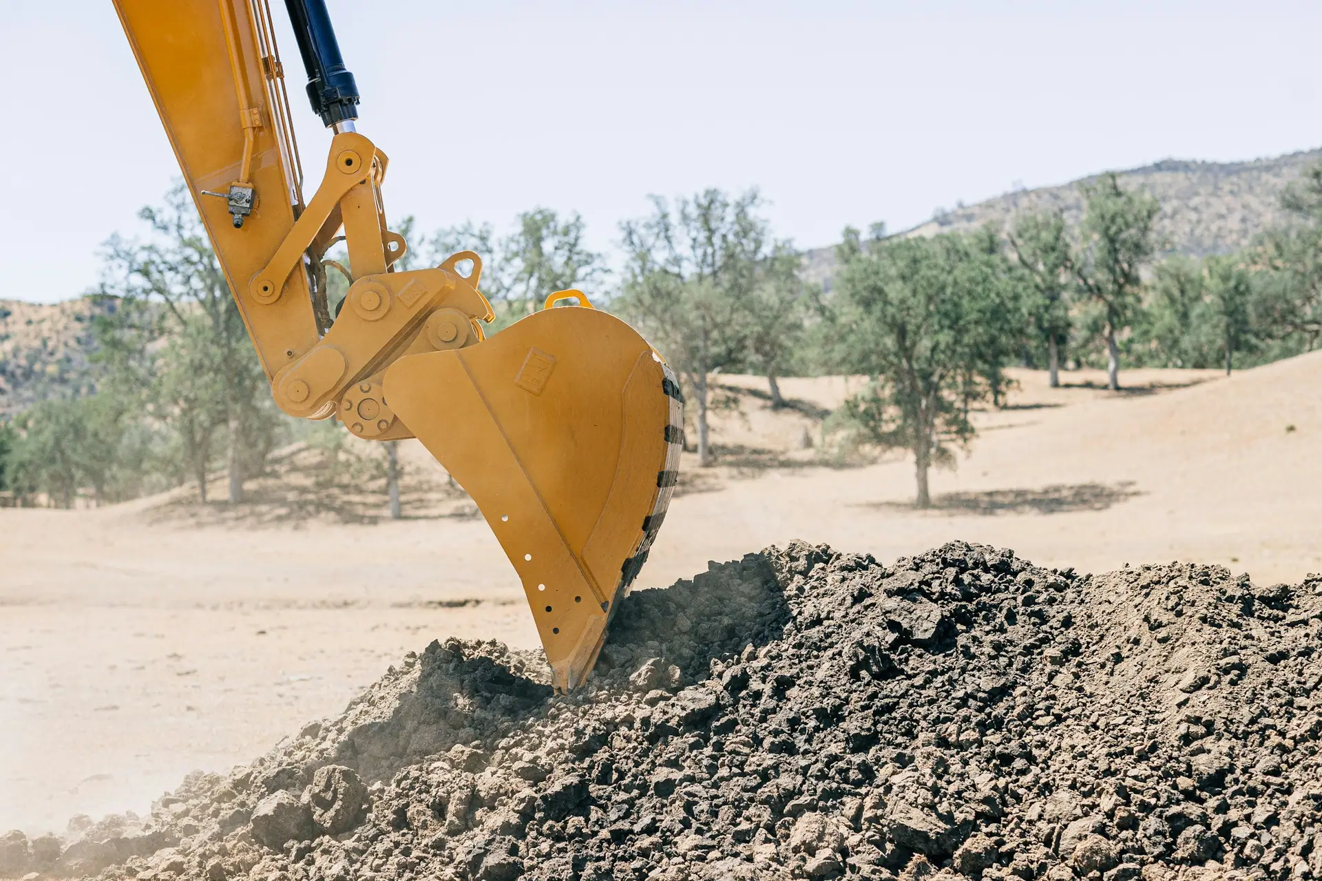 Excavator bucket digging into a pile of excavated soil