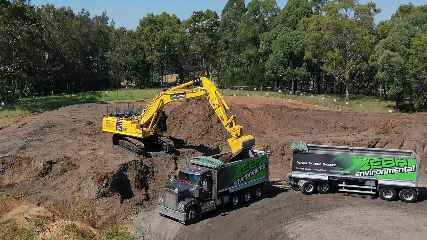 Excavator loading excavated soil into an EBH Environmental truck and dog trailer