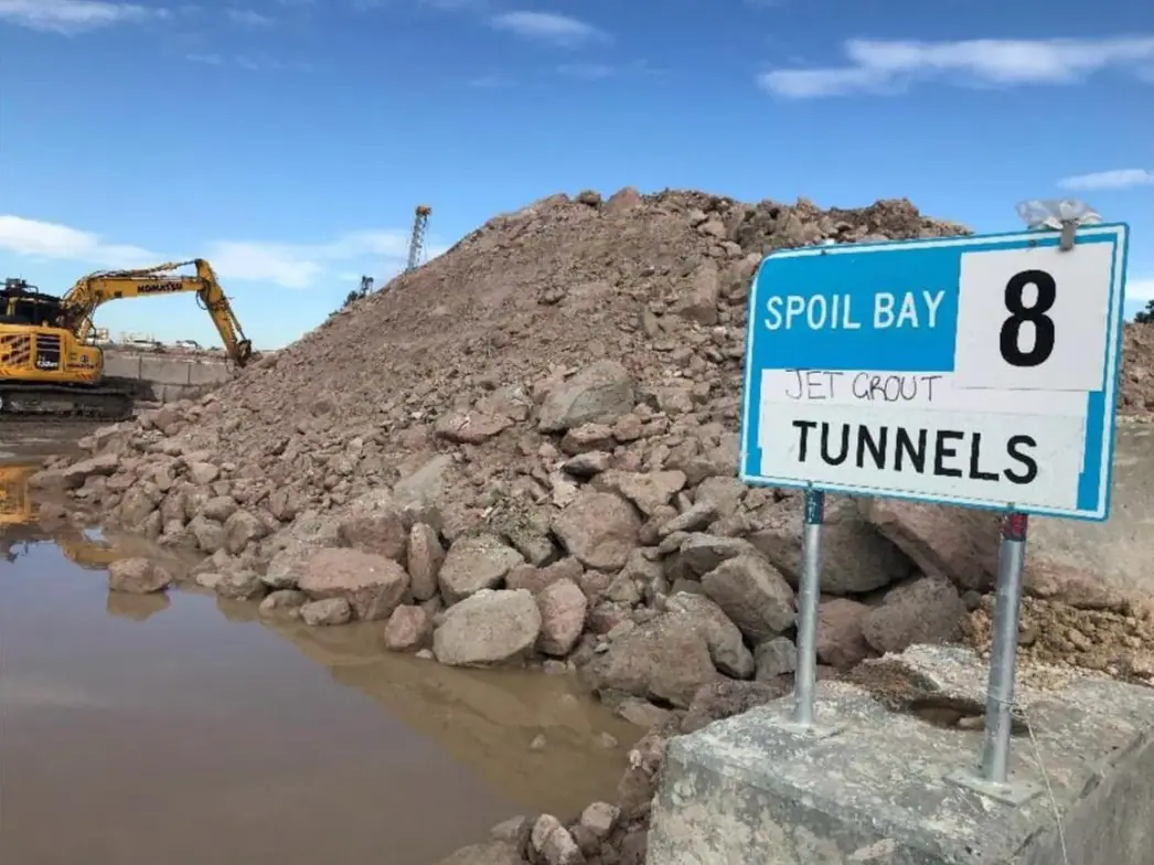 Spoil bay sign beside a stockpile of excavated rock, with an excavator behind