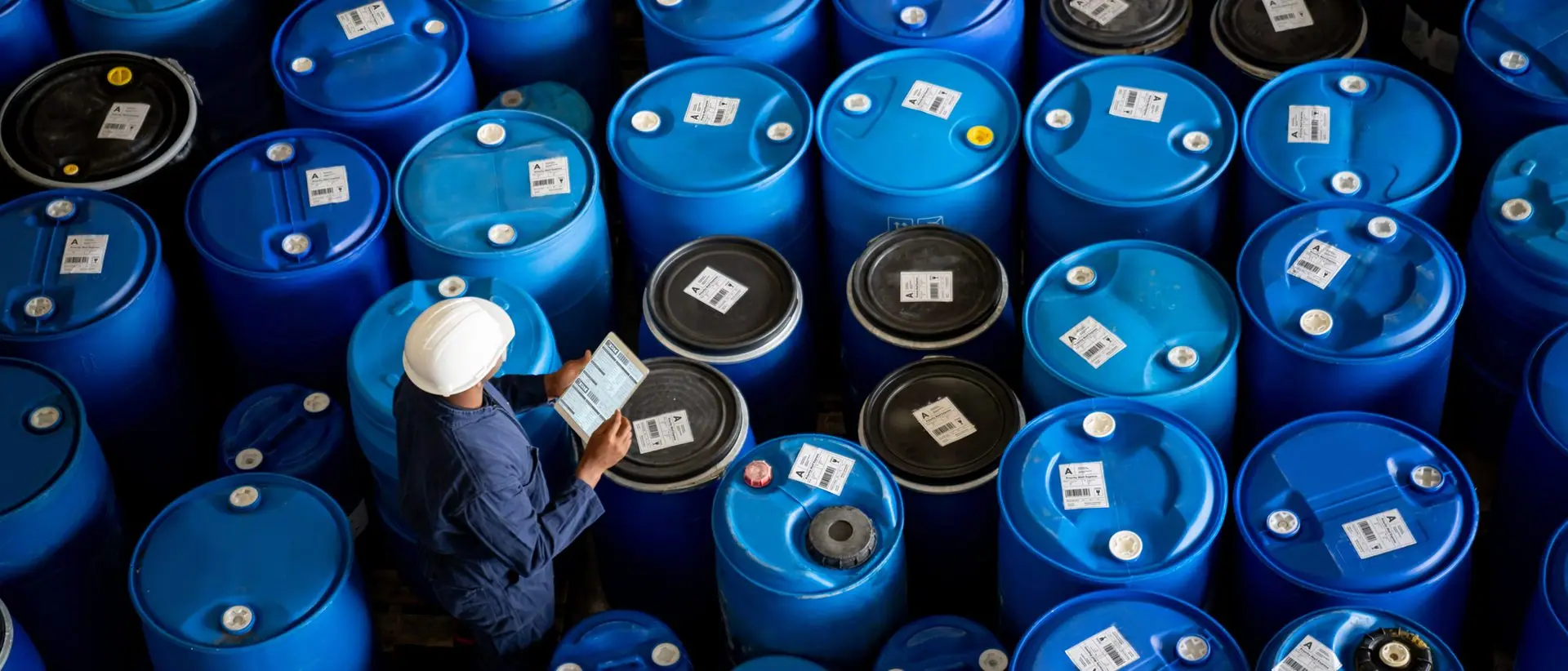 Worker checking stock of sealed chemical drums at an industrial plant