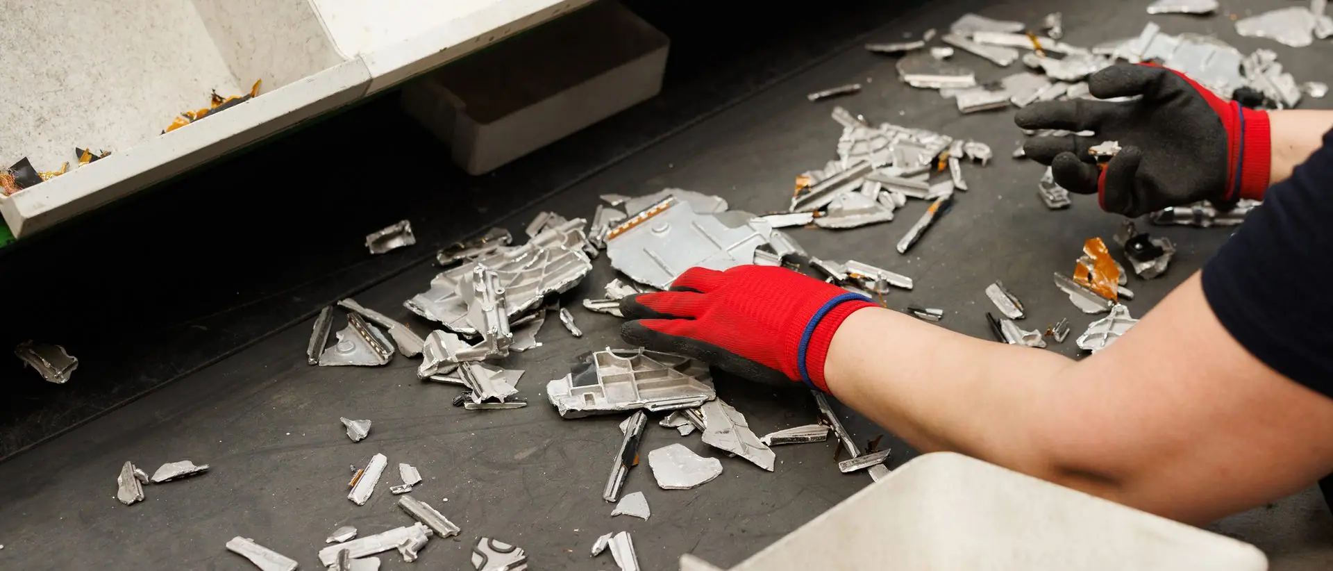 Gloved hands separating metals on a recycling sorting line